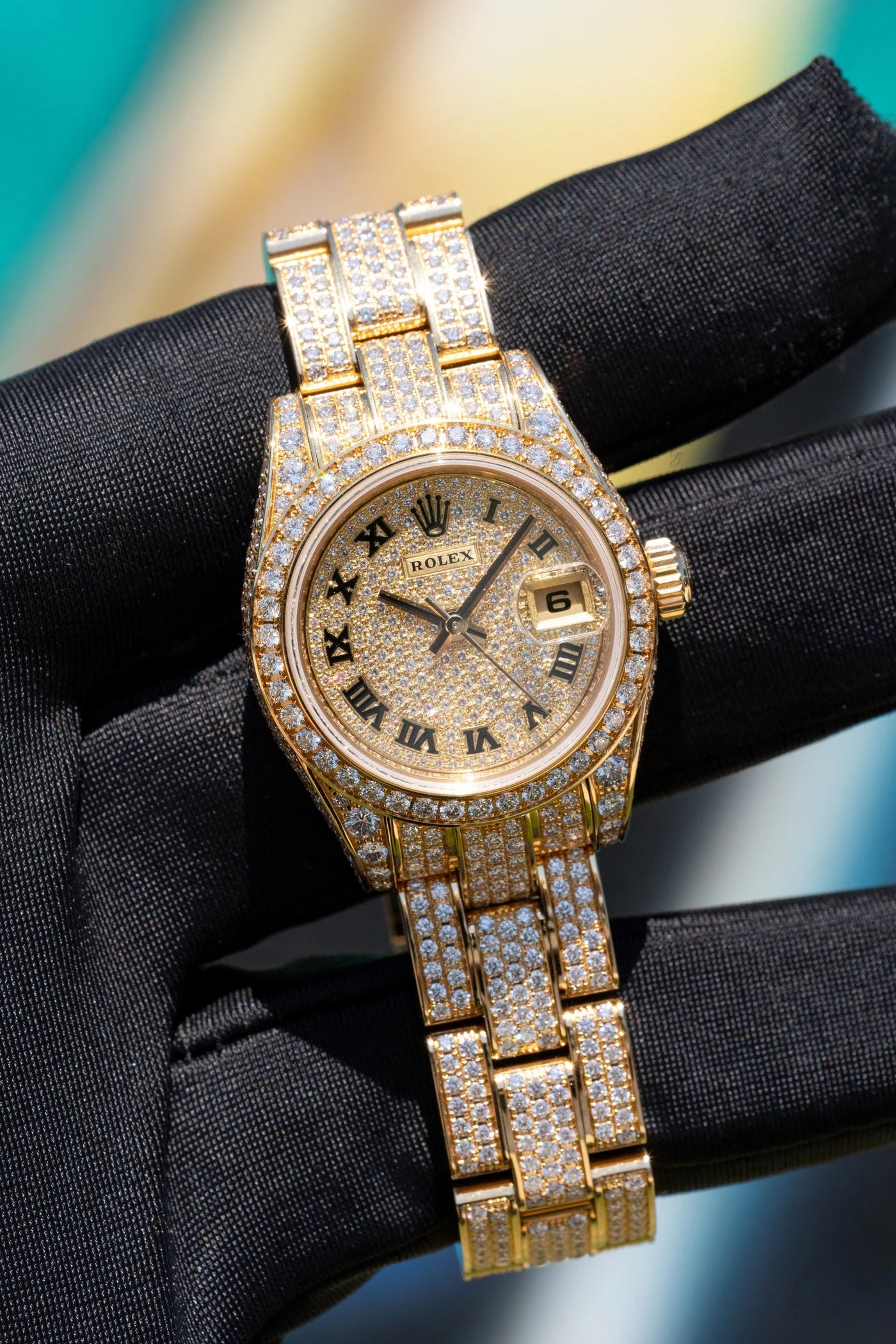 Gold tone Rolex watch covered with clear stones held in a black glove