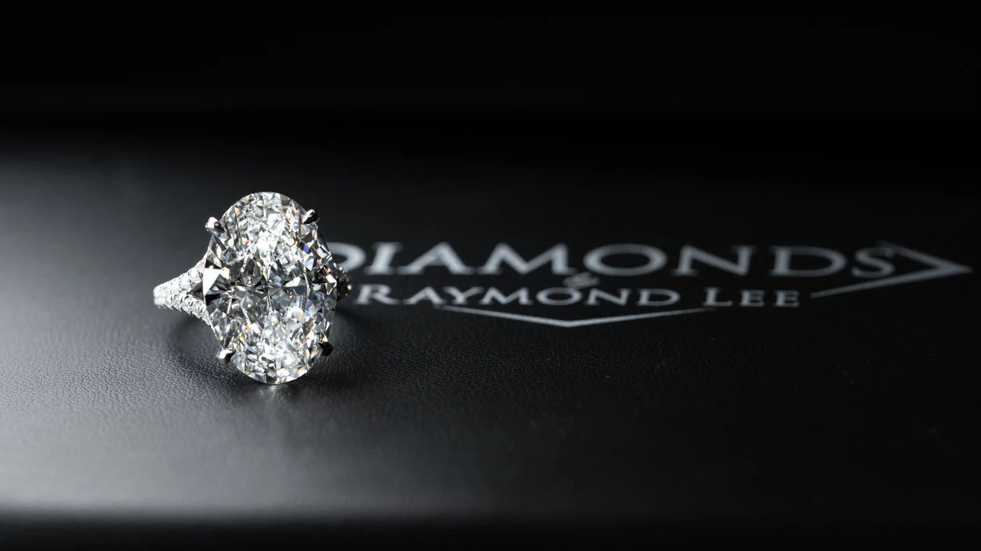 An oval diamond ring displayed on a black Diamonds by Raymond Lee presentation mat.