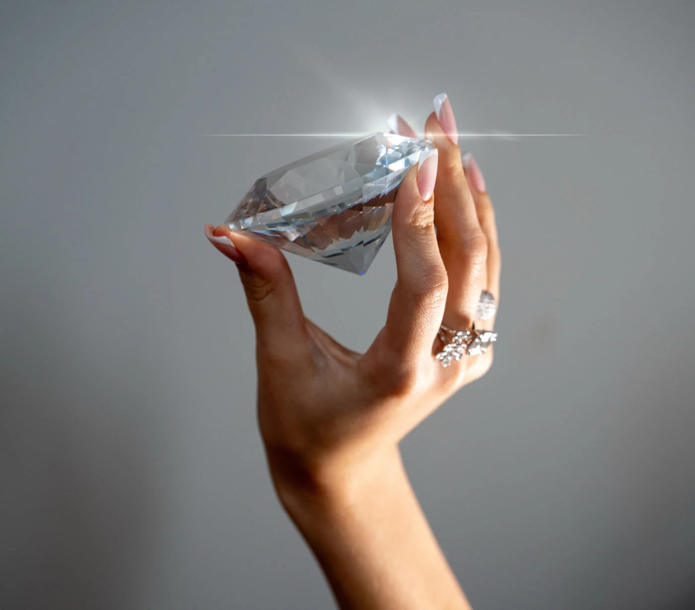Hand wearing rings while holding a clear faceted display stone against a gray background