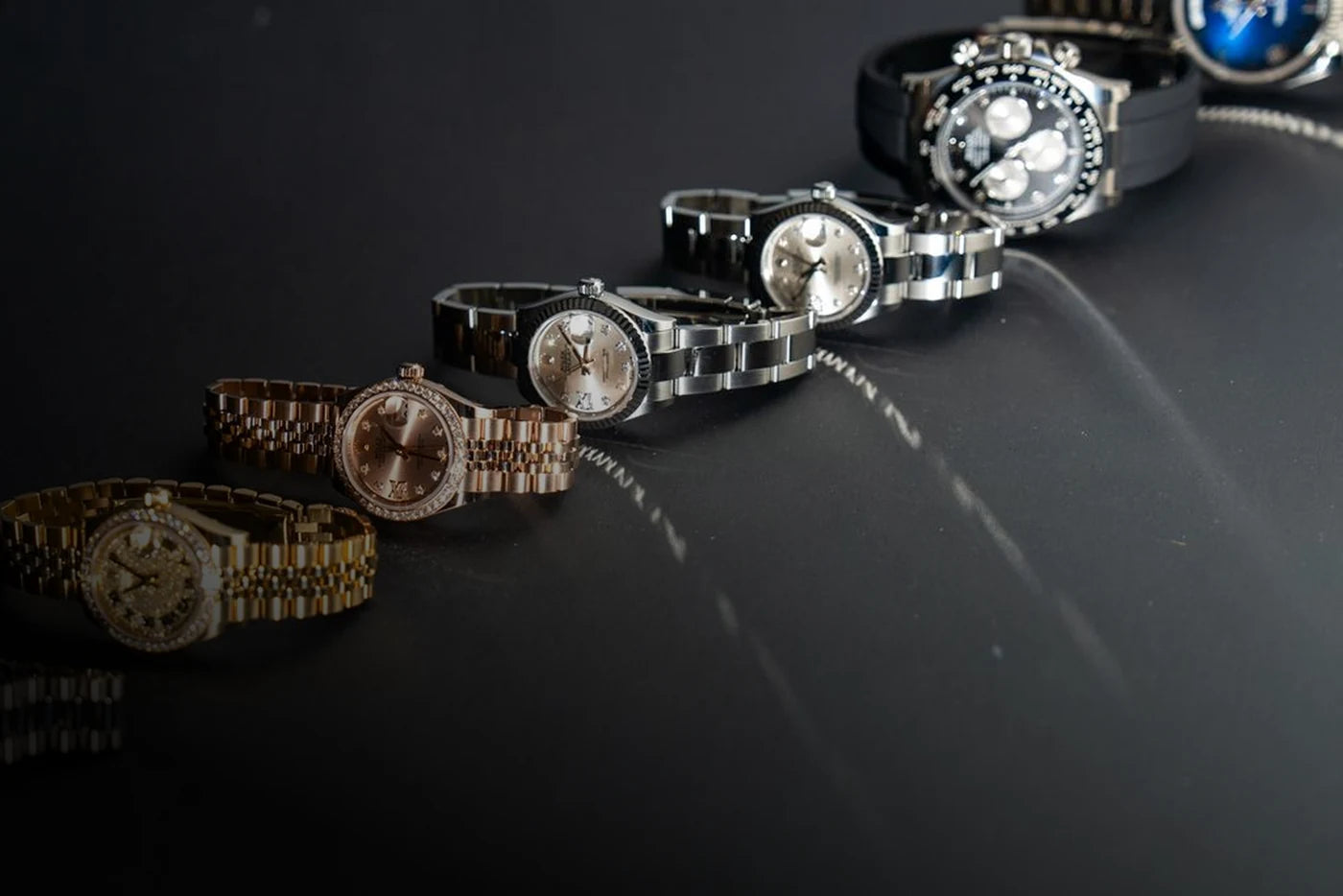 A row of gold, two-tone and steel watches on a dark display surface.