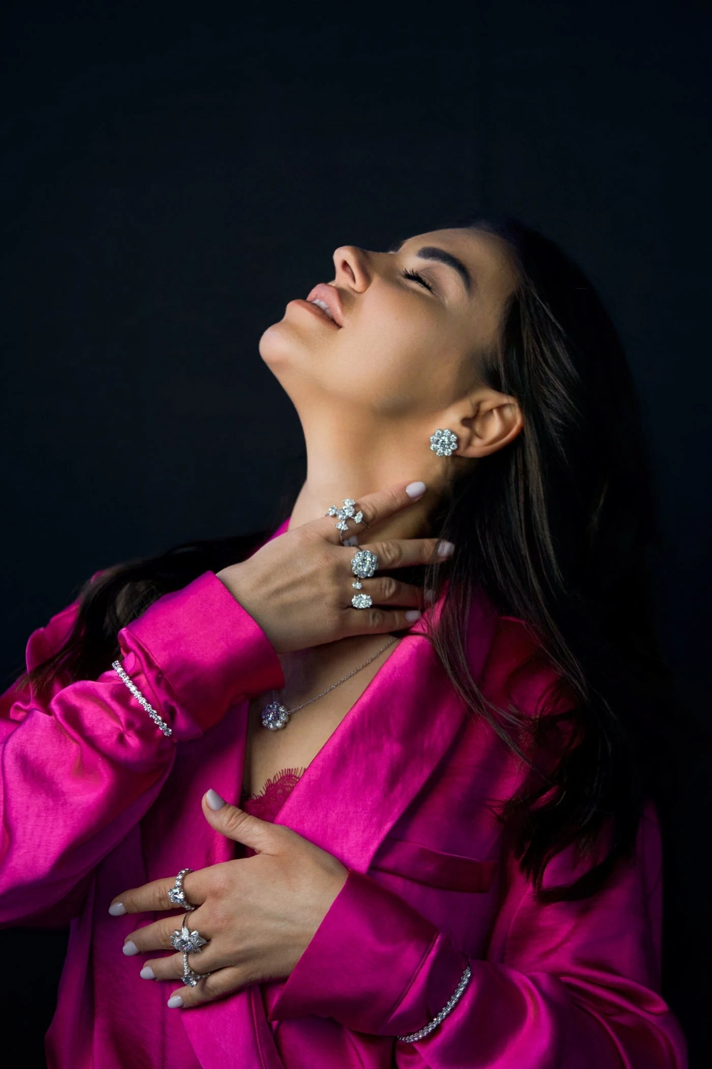 Model in a pink jacket wearing rings, earrings and a pendant necklace