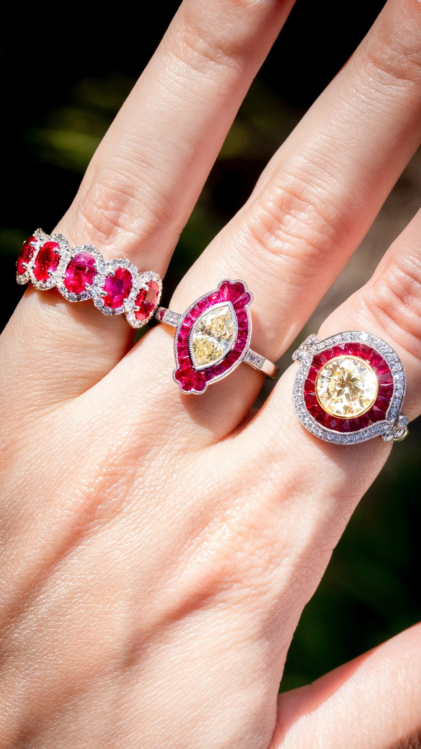 Three rings with red gemstones and contrasting center stones shown on a hand