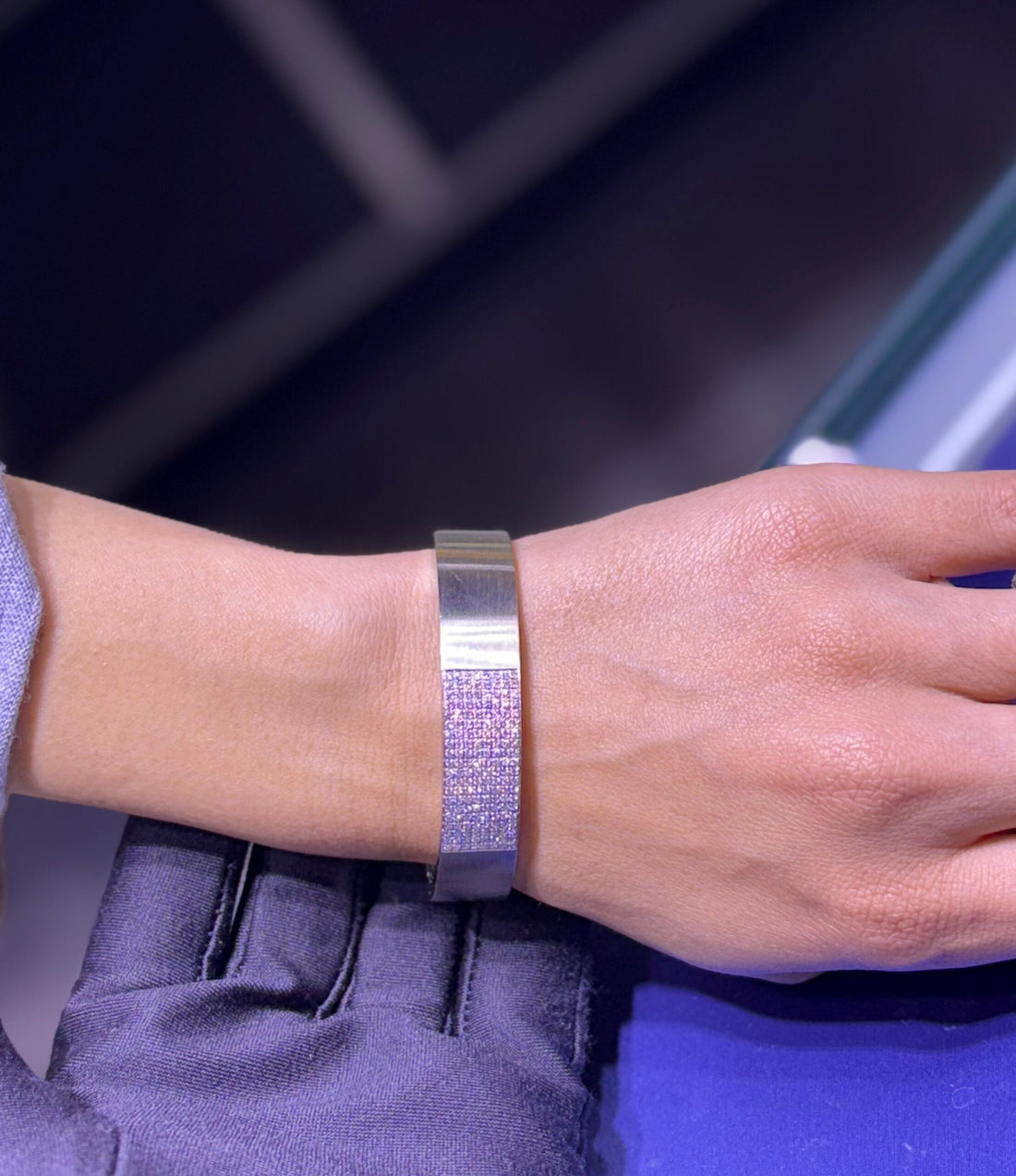 Wide metal cuff bracelet featuring a central strip of pavé-set pink or colorless square-cut stones on a wrist.