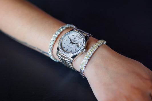 A Rolex Day Date with a light dial and stone set bezel worn between bracelets.