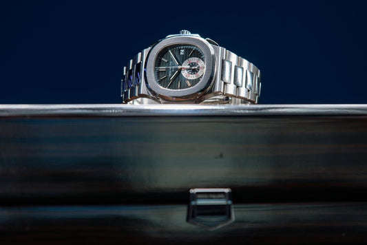A Patek Philippe Nautilus with a dark dial displayed above a case.