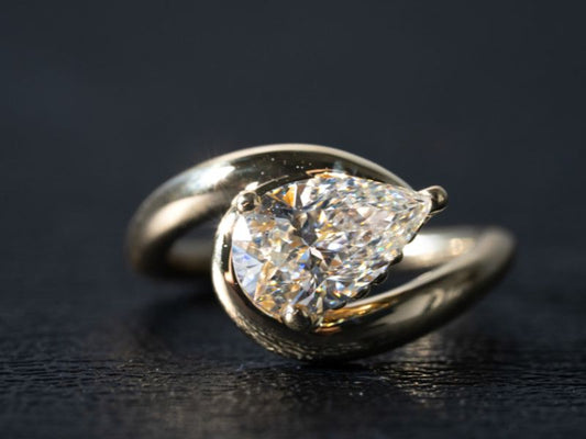  A close-up shot of a white gold or platinum ring featuring a brilliant pear-shaped diamond set in a modern tension or bypass style setting on a dark background.