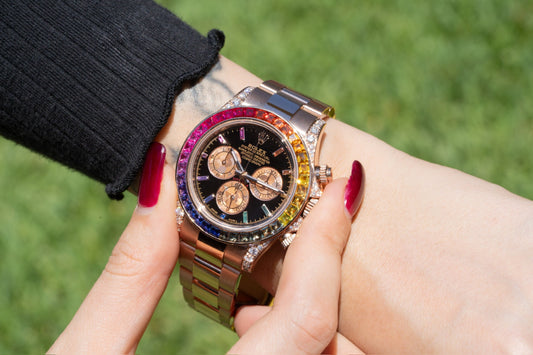 close-up of a person wearing a luxurious gold rolex watch with a rainbow gemstone bezel outdoors.