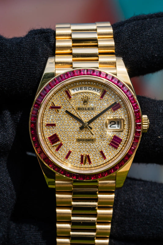 Close-up of a Rolex Day-Date watch in yellow gold, featuring a fully diamond-paved dial, baguette-cut ruby hour markers, and a ruby-set bezel. The gold President bracelet enhances the timepiece’s opulent and regal design.