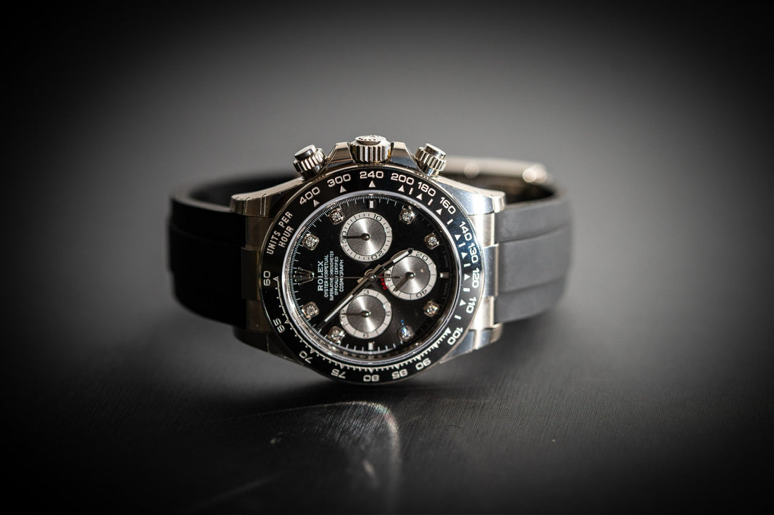 close-up of a black dial rolex daytona with a black rubber strap displayed on a dark surface.