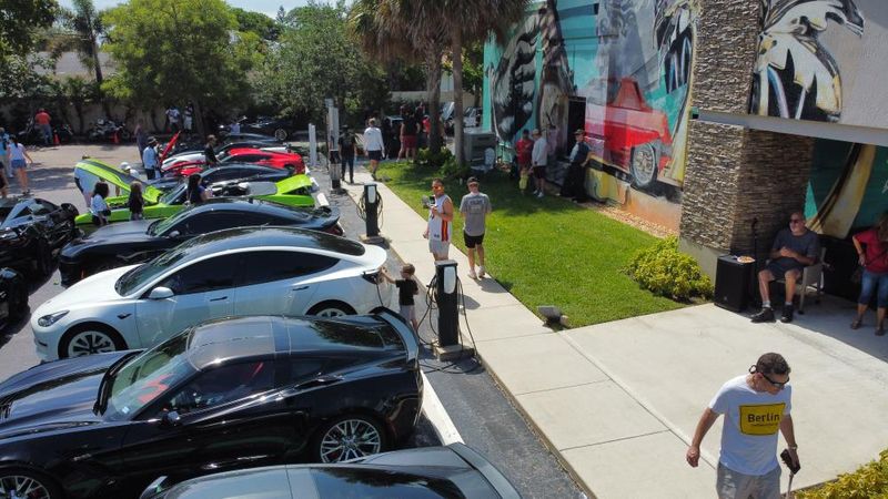 Cars and visitors outside the showroom during a gathering.