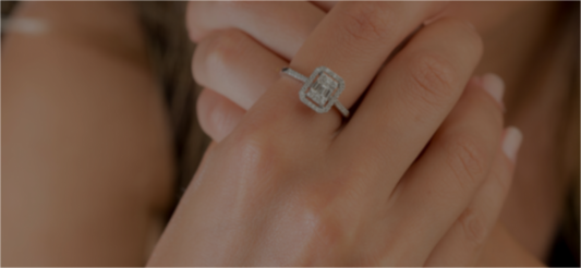 A rectangular center stone ring with a halo of smaller stones, worn on a finger.