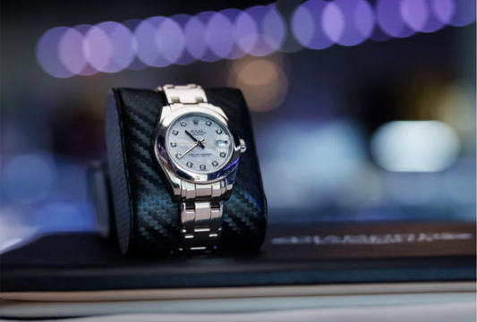 A Rolex watch with a light dial displayed on a cushion.