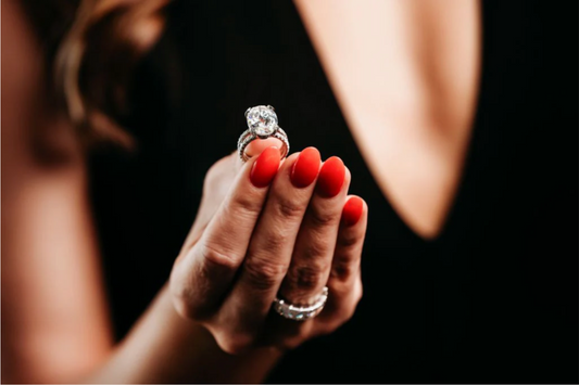 A large clear stone ring held between fingertips.
