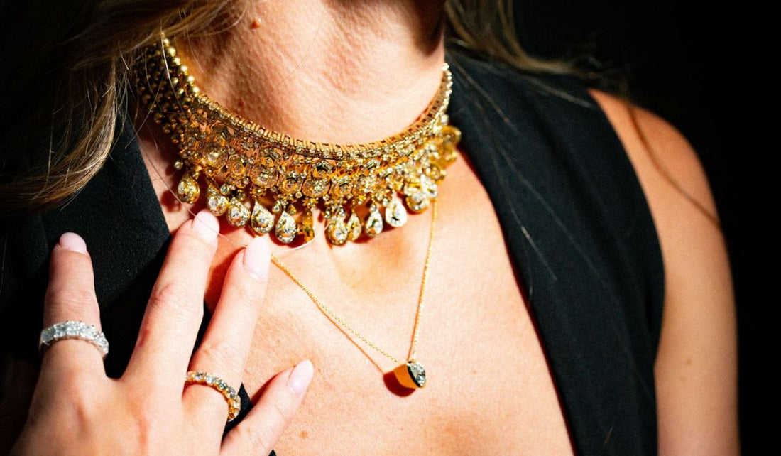 An ornate gold tone necklace with hanging drops worn above a smaller pendant.