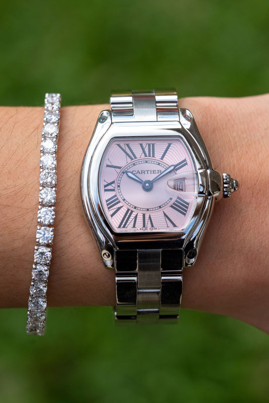 Cartier Roadster with a pink toned Roman numeral dial worn beside a stone bracelet.