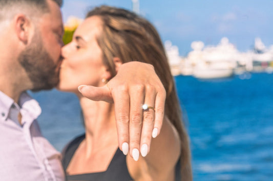 A couple beside the water showing an engagement ring.