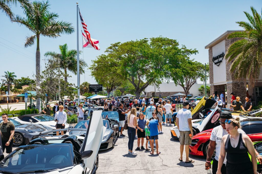 A gathering of visitors and cars outside the showroom.