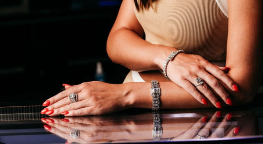 Woman's hands with red manicure, diamond bracelets, and rings resting on a reflective surface.