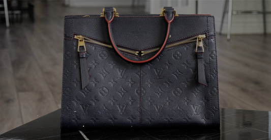 A dark Louis Vuitton tote with an embossed monogram and two front zippers.