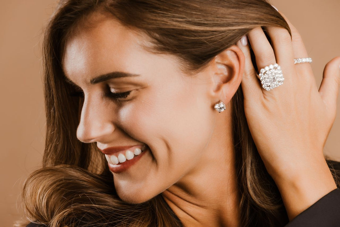 Portrait of a smiling woman showcasing fine diamond jewelry: stud earrings, a prominent cocktail ring, and a pave diamond band.