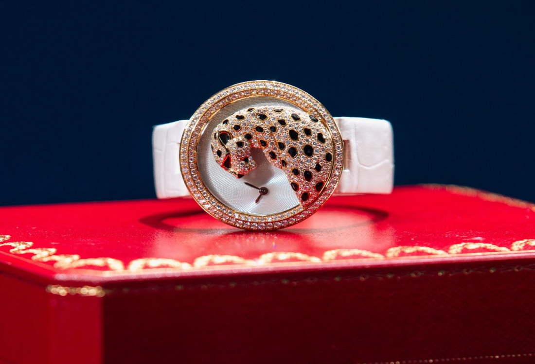 Luxury Cartier diamond-studded panther watch displayed on a red jewelry box. Features a white strap and gold case with intricate black-spotted panther design.