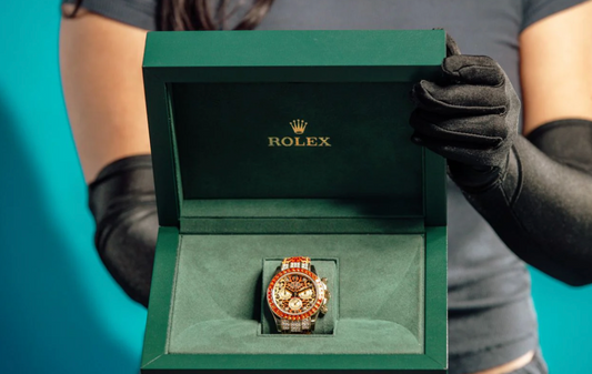 A stone set chronograph with a red bezel displayed in a green Rolex presentation box.