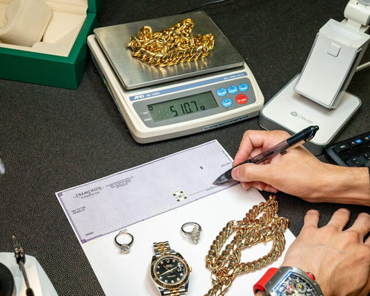 A gold tone chain on a scale beside rings, a watch and a check being written.