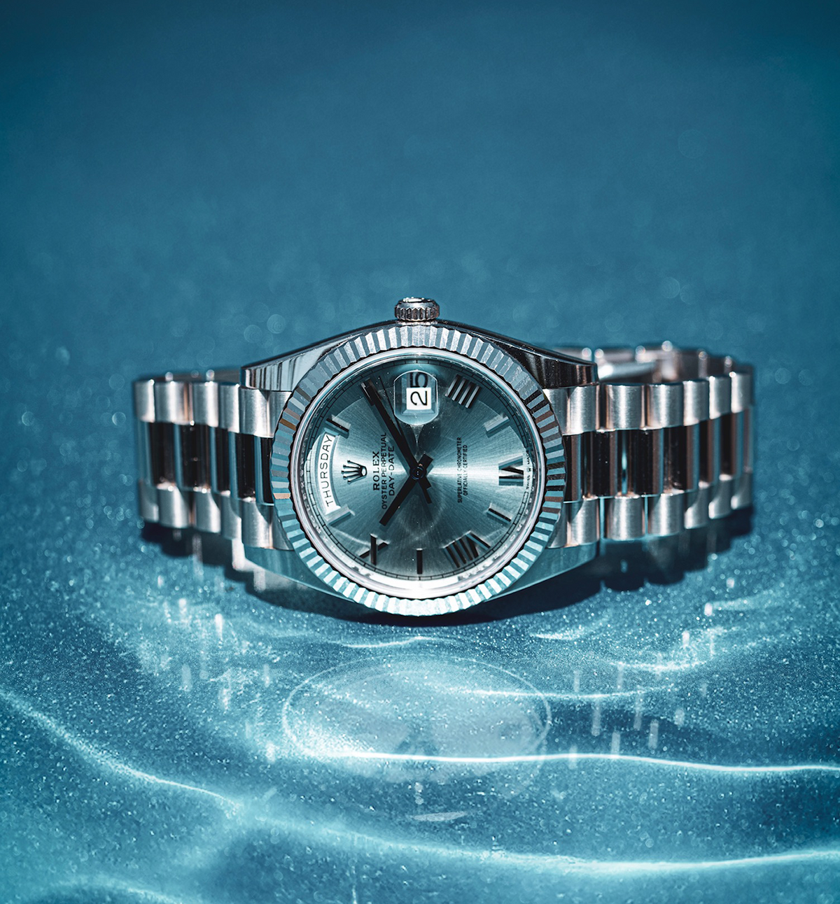 Rolex watch with a blue dial and metal bracelet on a blue surface