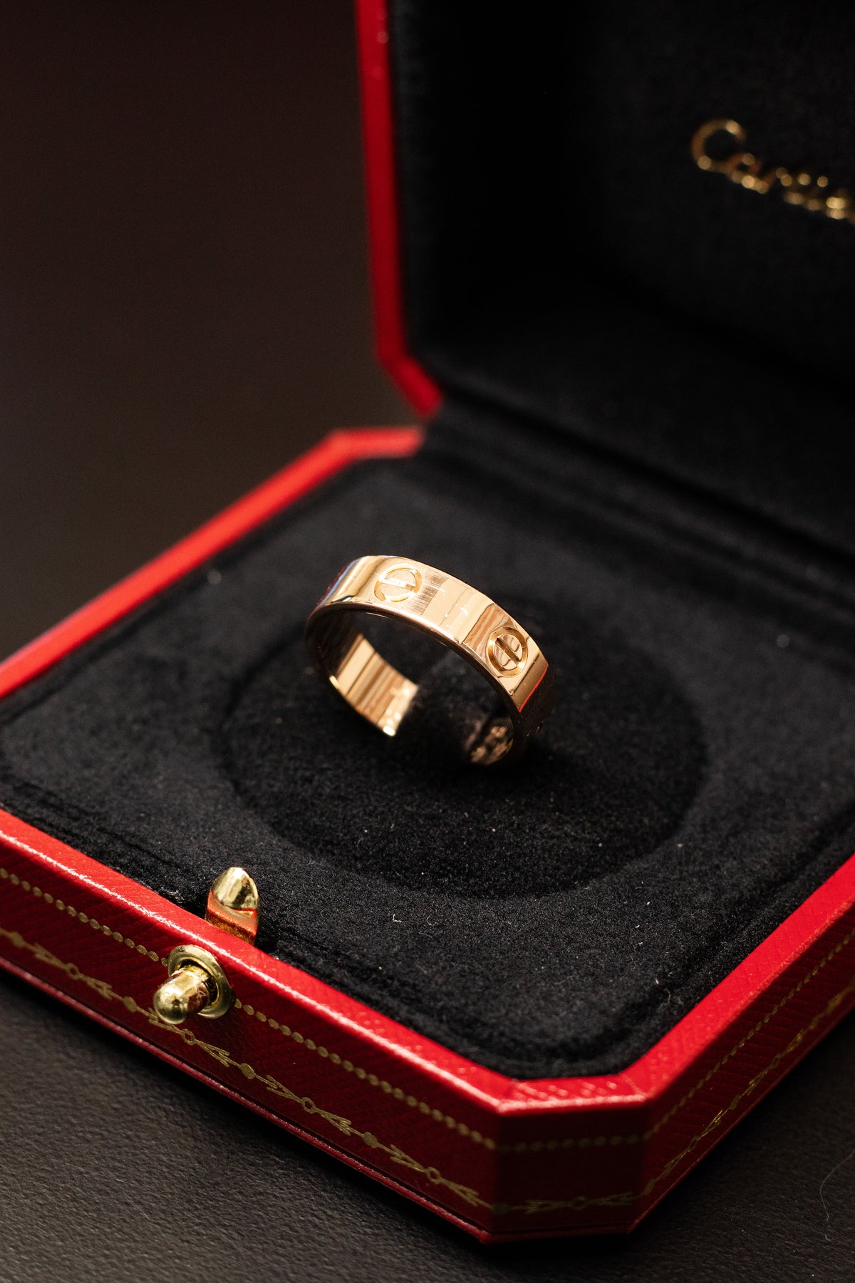 Gold tone ring with screw motifs displayed in an open red Cartier box