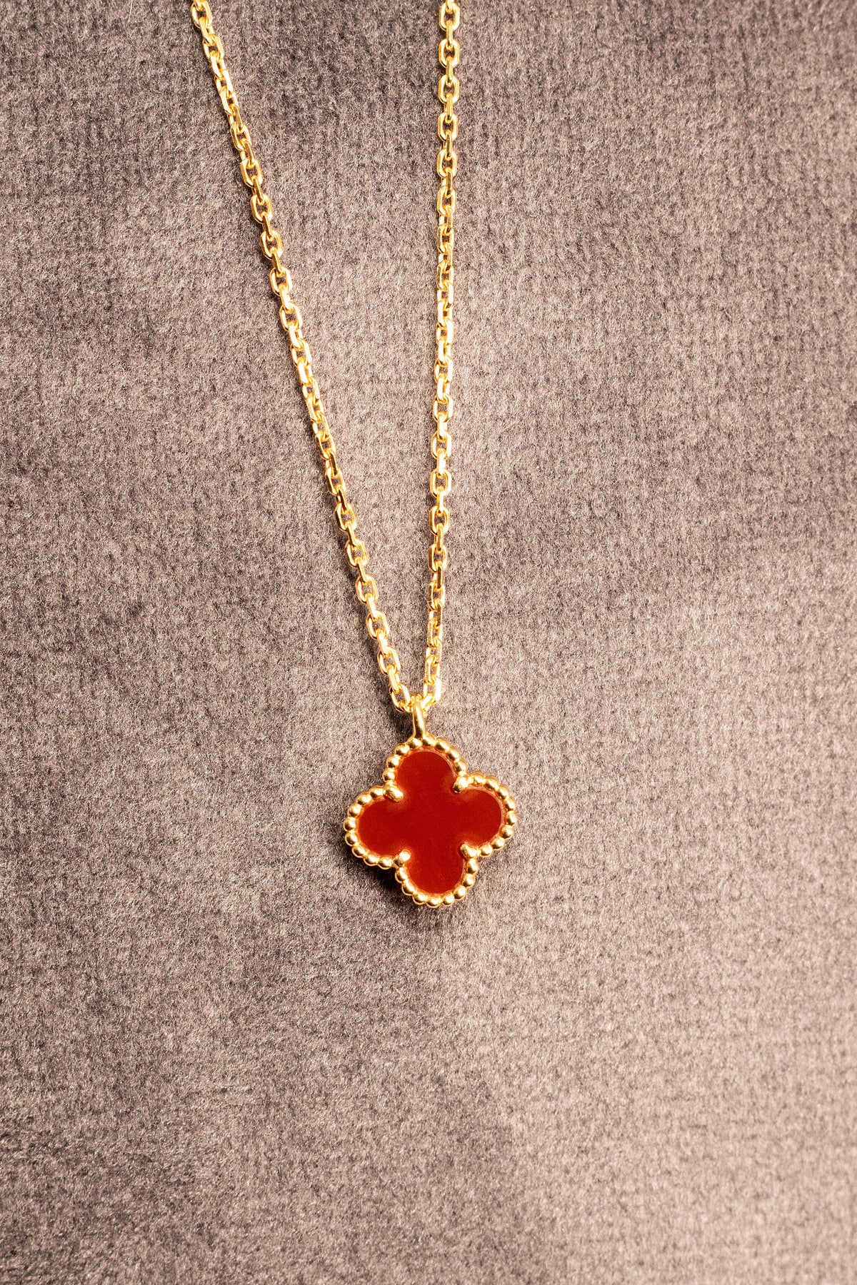 Red clover motif pendant on a gold tone chain against a gray background