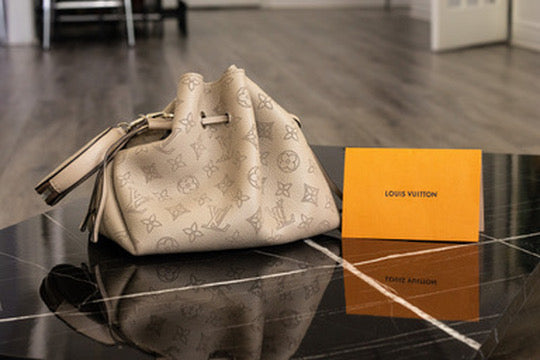 Cream Louis Vuitton monogram bucket bag beside an orange booklet