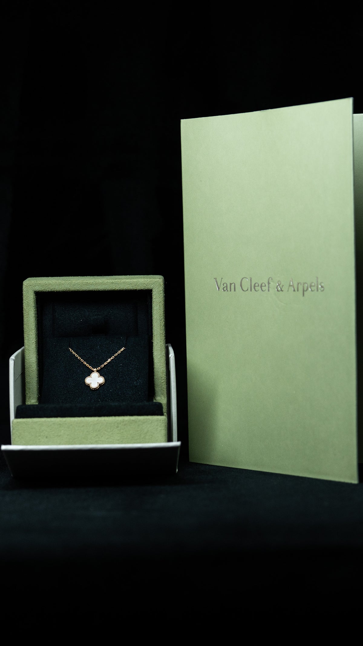 White clover motif pendant in a green jewelry box beside Van Cleef & Arpels packaging