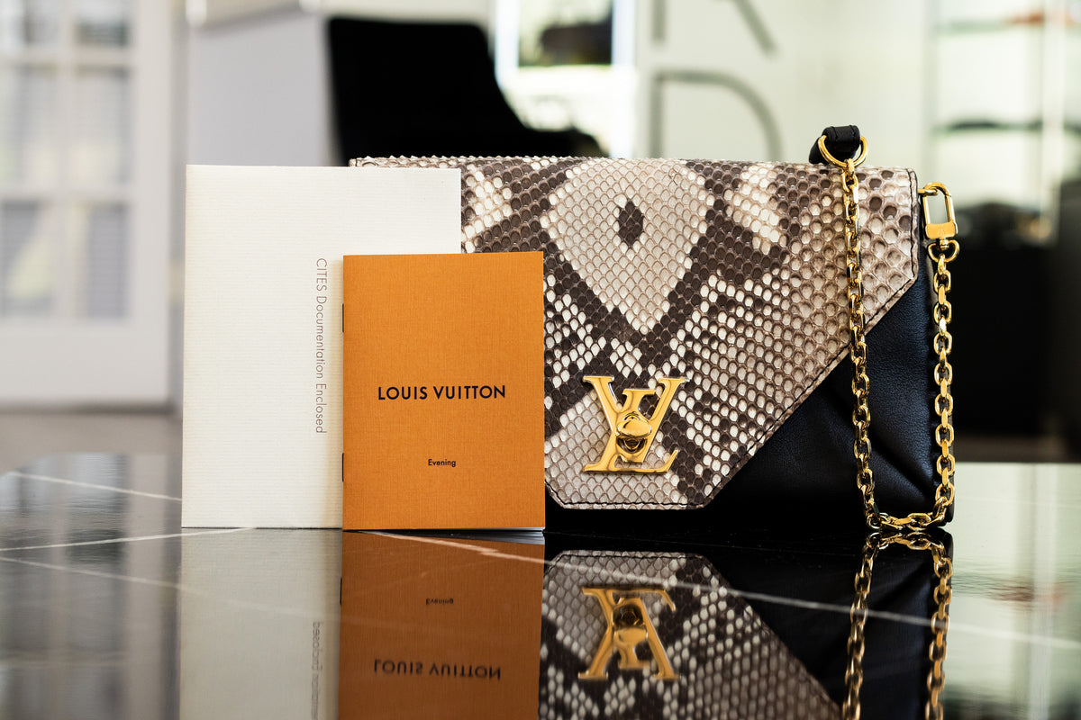 Louis Vuitton bag with a patterned flap and gold tone chain beside its documentation