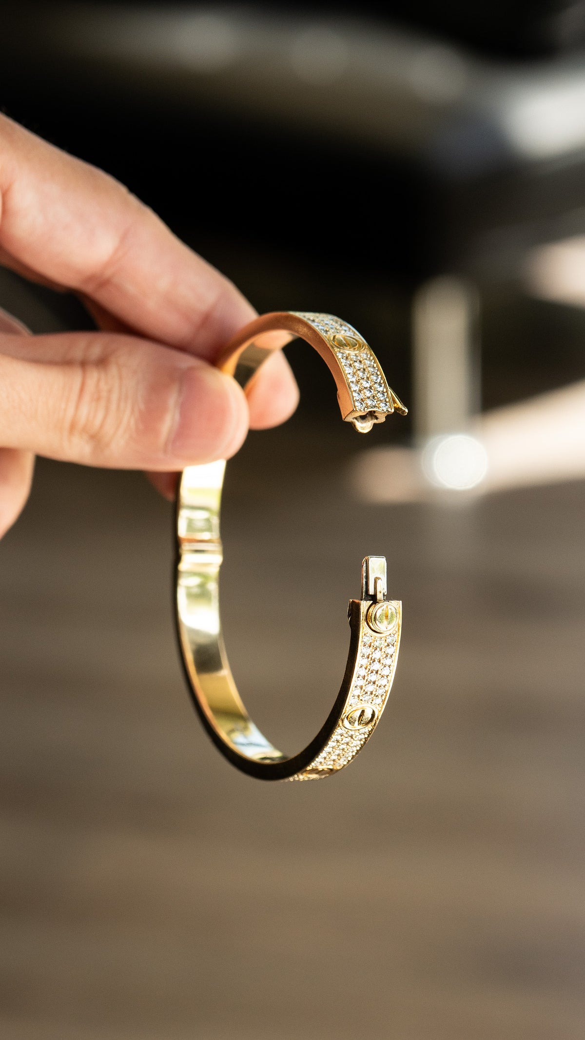 Open gold tone bracelet with rows of clear stones and screw motifs held in a hand