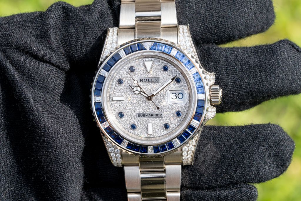 Rolex watch with a stone set dial and blue stone bezel held in a black glove