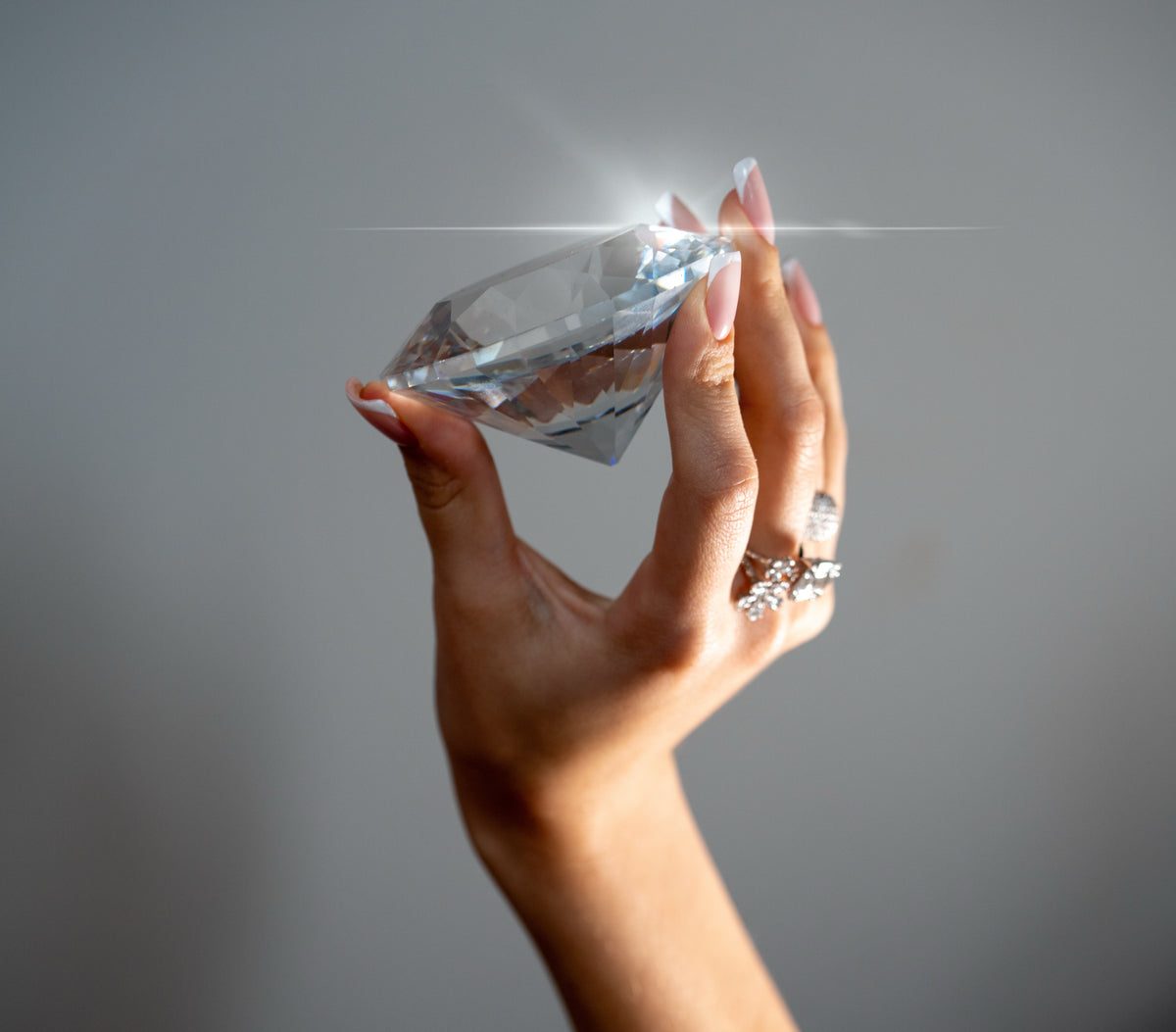 Hand wearing rings and holding a large faceted clear display stone