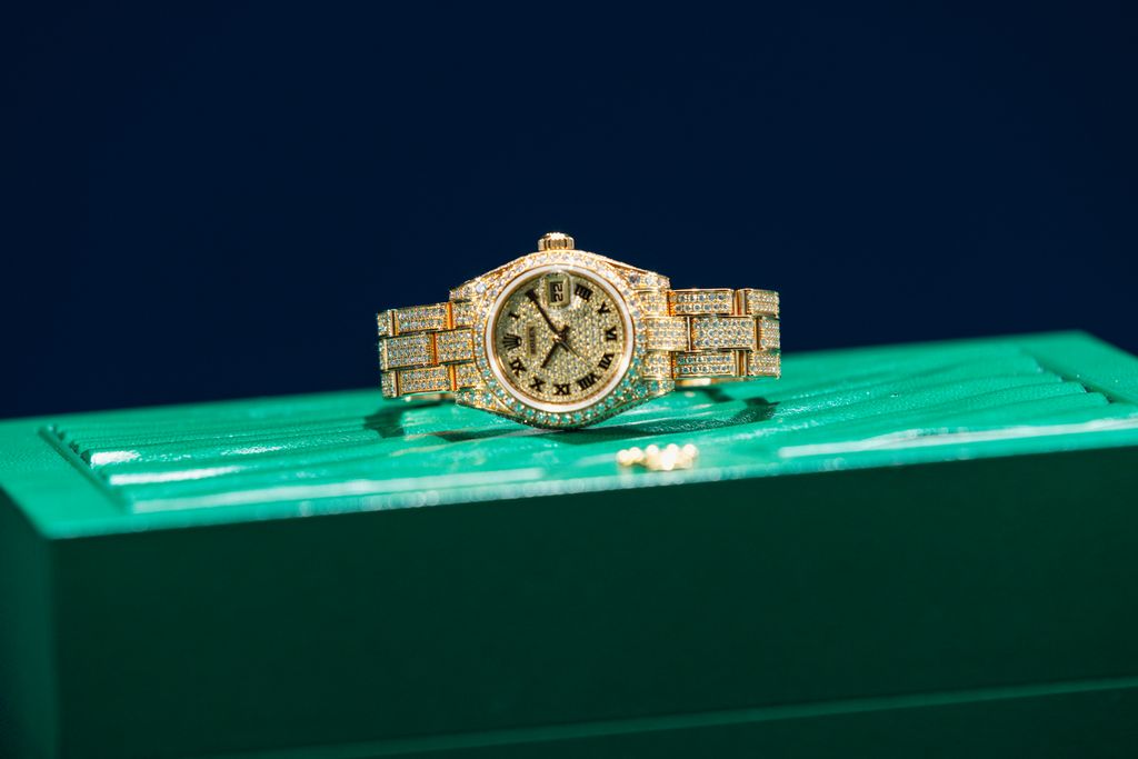 Gold tone Rolex watch with a stone set dial and bracelet on a green box