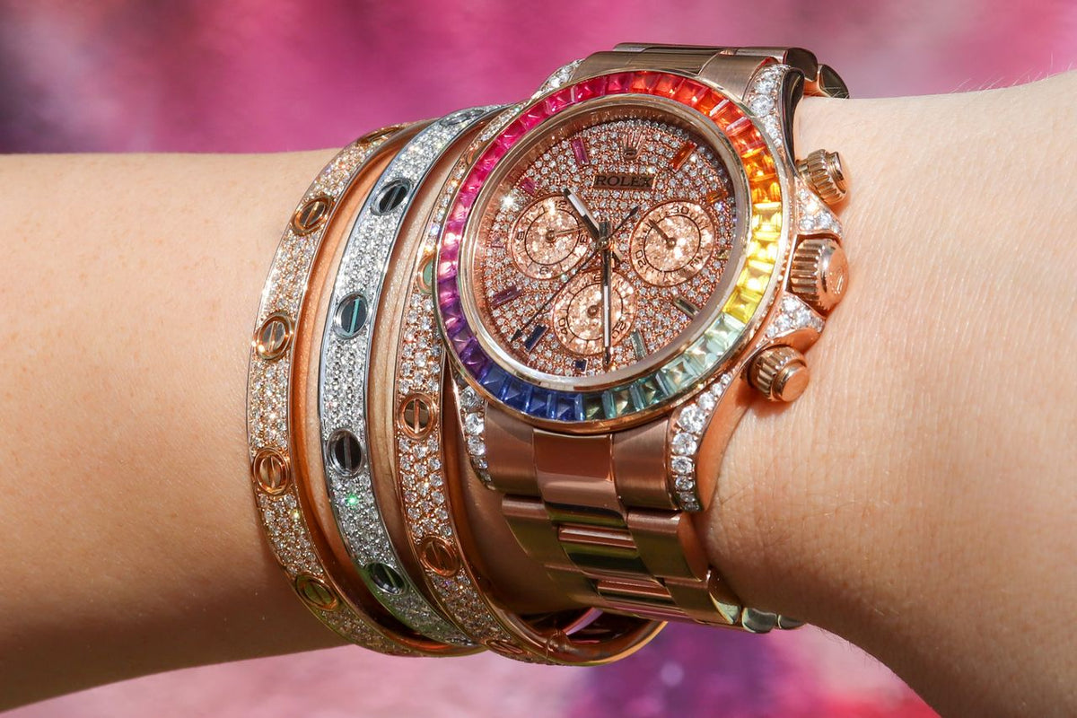 Rolex chronograph with a colorful stone bezel worn beside bracelets