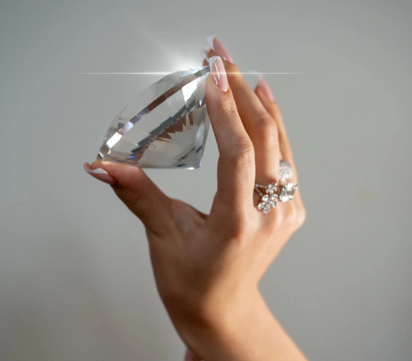 Close view of a hand holding a clear faceted display stone beside rings