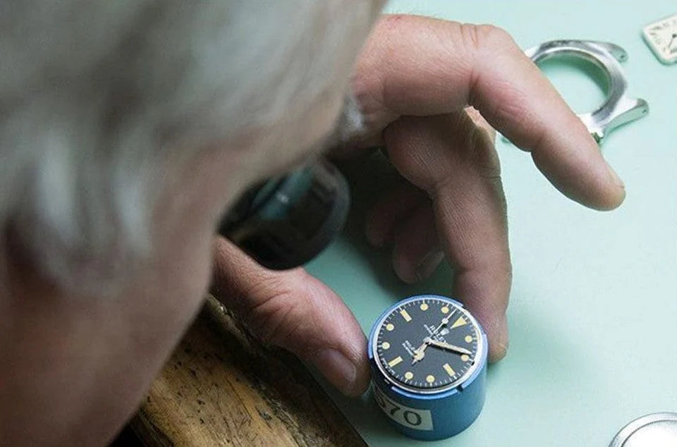 Hands examining a watch dial at a workbench