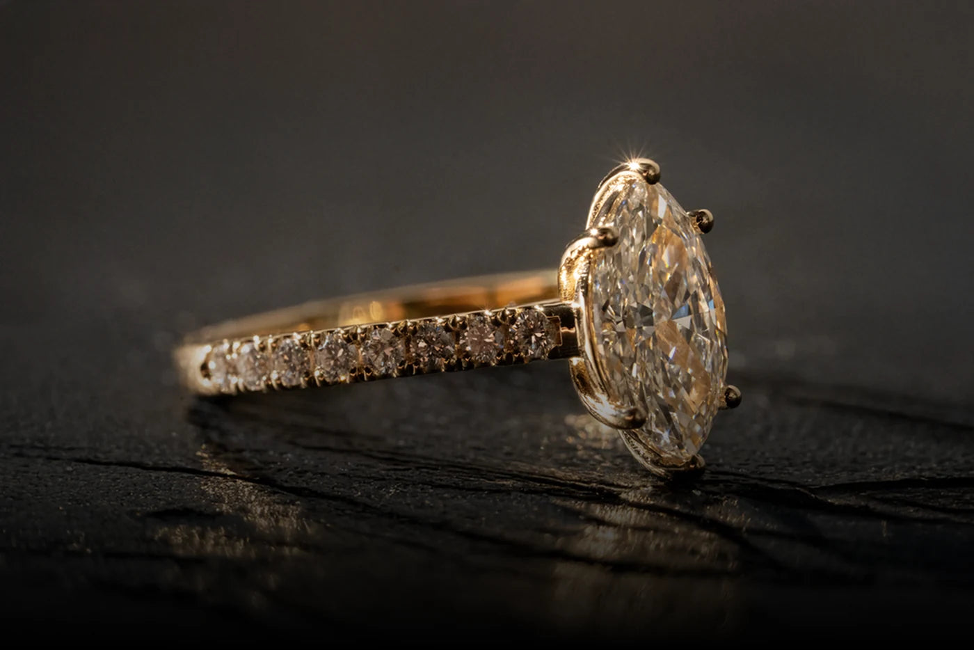 A side view of an oval diamond ring in yellow gold with a diamond-set band.