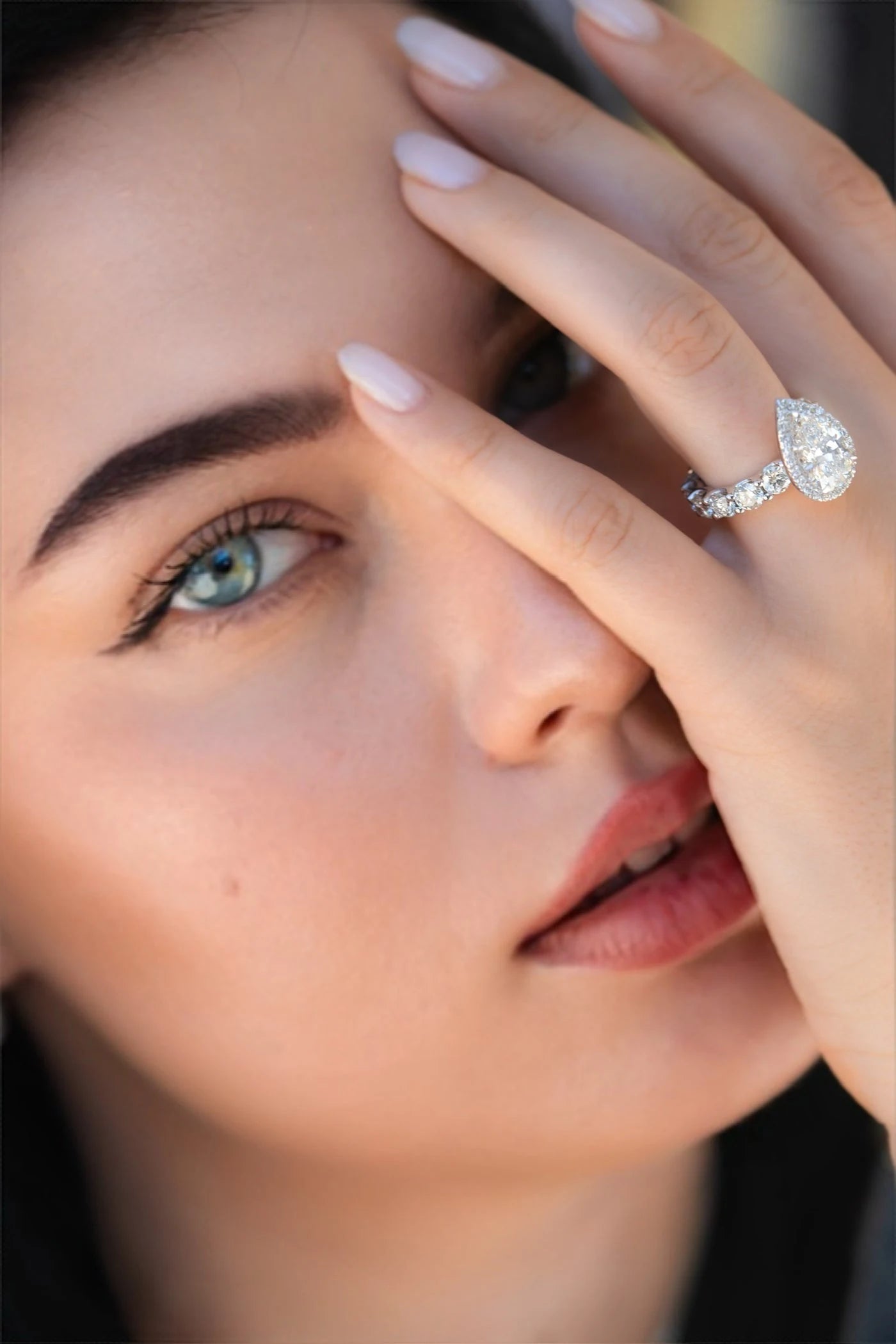 Model wearing a pear shaped ring with her hand beside her face