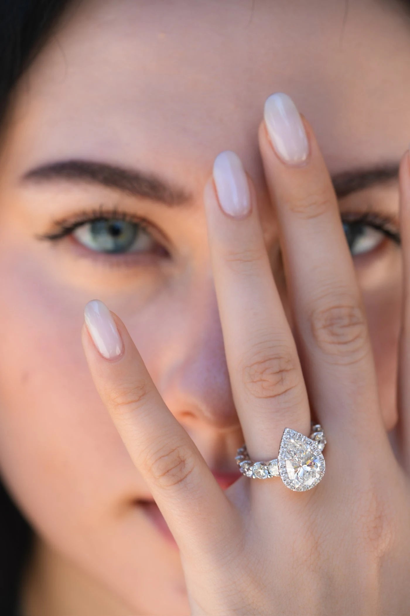Close view of a pear shaped ring on a hand held in front of a face