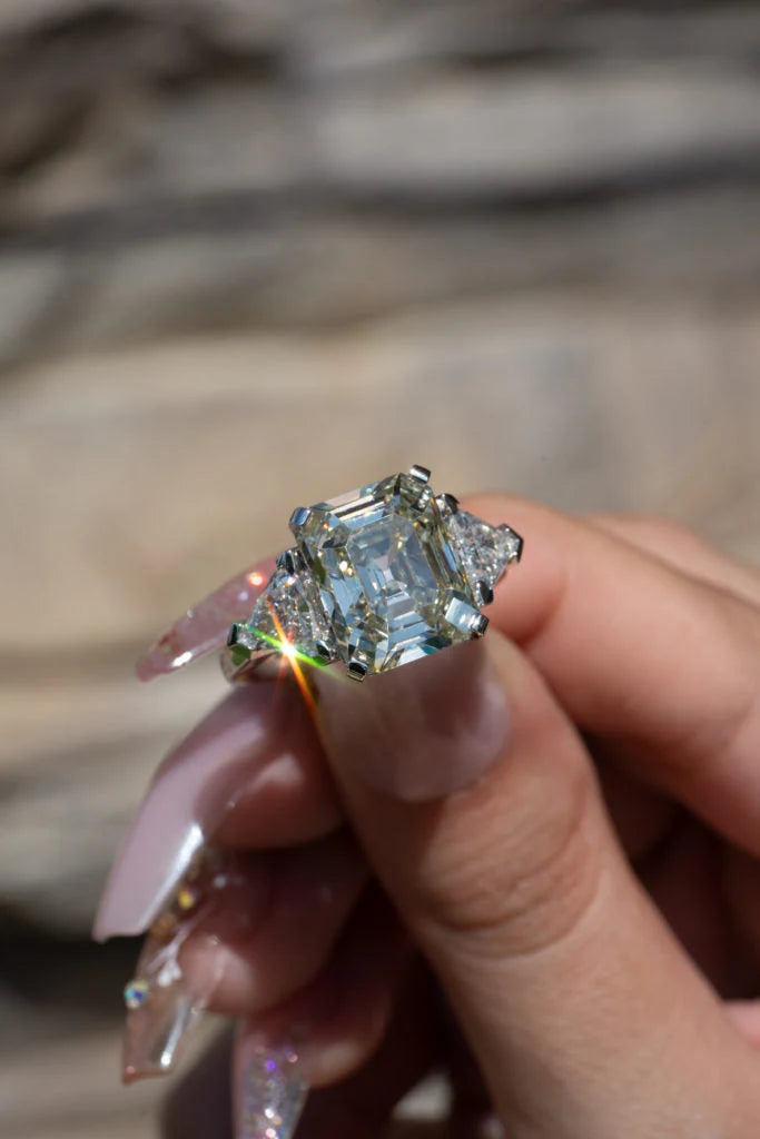 Rectangular center stone ring with side stones held between fingers