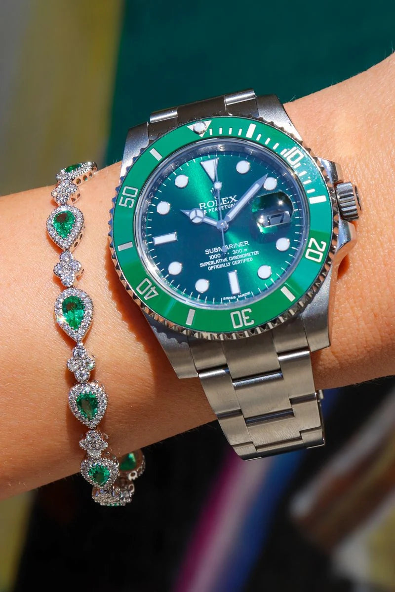 Rolex Submariner with a green dial worn beside a bracelet with green and clear stones