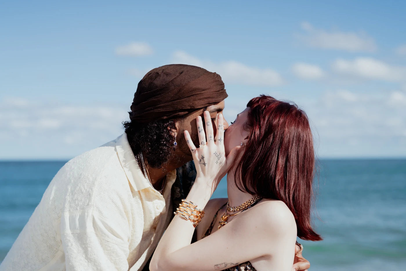 Couple kissing beside the ocean with an engagement ring visible