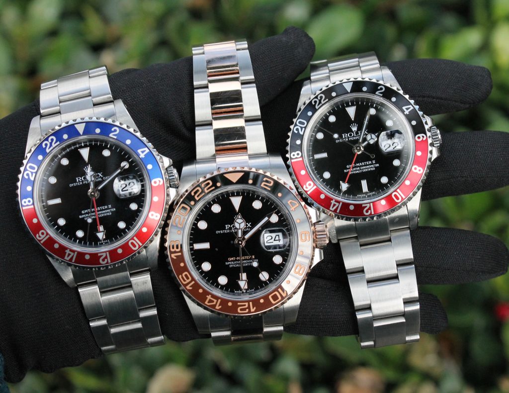 three watches held together left to right: Rolex Pepsi , Rolex GMT Master Root Beer, and Rolex GMT Master II Coke (not pictured but compared in article Rolex GMT Master 2 Batman)