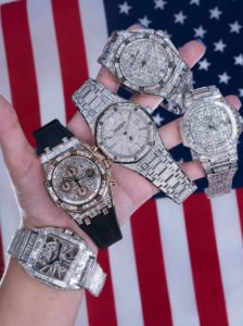A hand holding five iced-out luxury sport watches in front of an American flag, representing affordable watch style under $500.