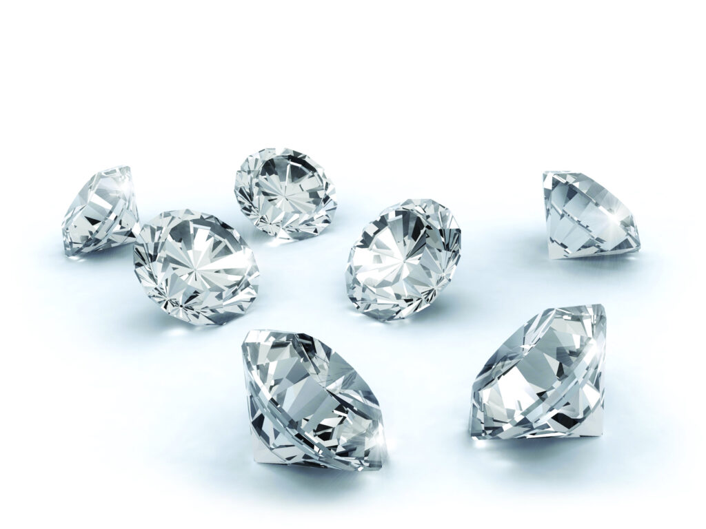 Hand showcasing multiple luxurious rings featuring natural diamonds against a green outdoor background.